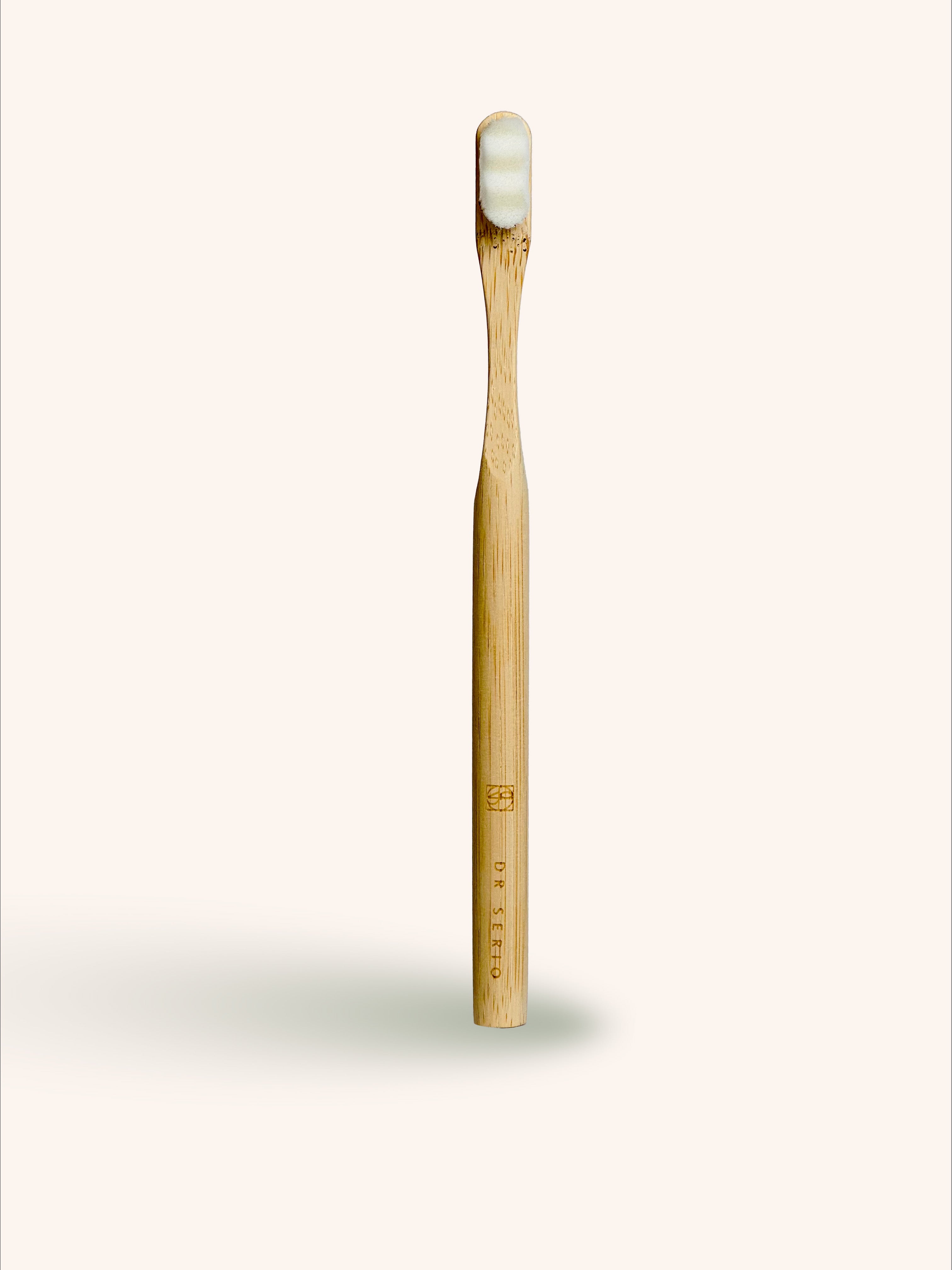 A bamboo toothbrush with a soft head, featuring white bristles and a wooden handle.